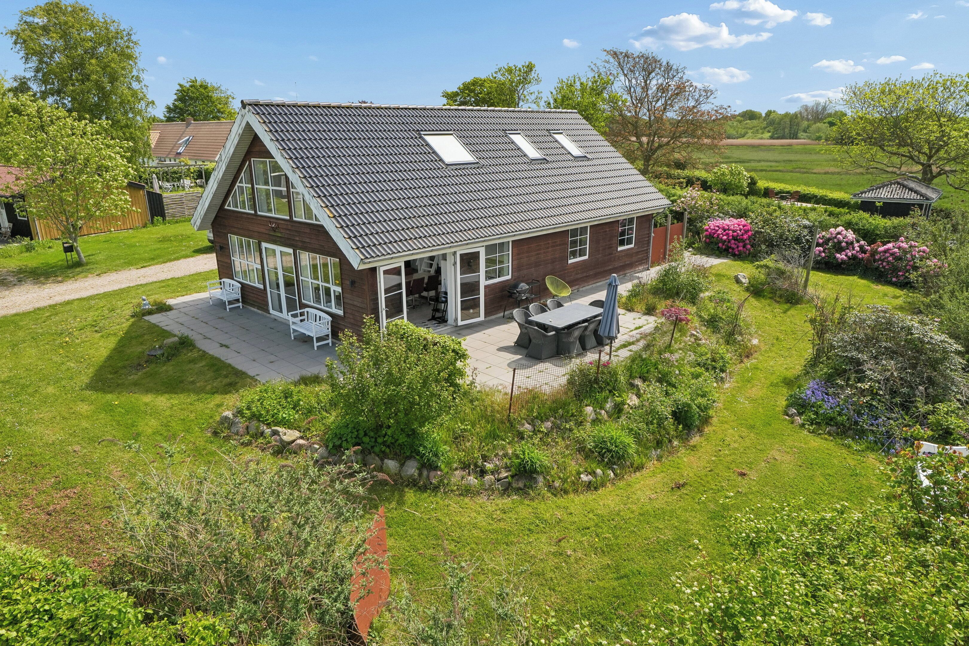 Een tweelaags huis met een schuin dak, grote ramen en een terras met buitenmeubilair.