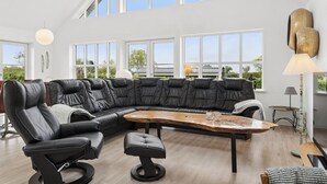 A modern living room with a black leather sectional sofa, a wooden coffee table, and a large window offering a view of the outdoors. - Scenic holiday home close to the water (Brenderup)