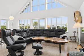 A modern living room with a black leather sectional sofa, a wooden coffee table, and a large window offering a view of the outdoors. - Scenic holiday home close to the water (Brenderup)