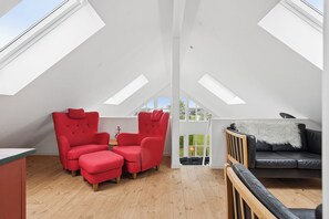 Ein Zimmer mit hohen Decken und Dachfenstern, ein roter Sessel, eine schwarze Couch und eine Holzbank.