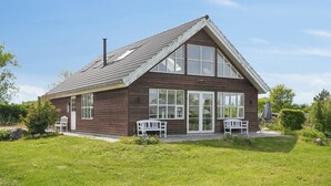 A wooden building with a gabled roof, large windows, and two white benches outside. - Scenic holiday home close to the water (Brenderup)