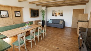 Un interior moderno con una mesa de comedor de madera, sillas con cojines verdes, un sofá gris y vigas de madera en el techo.