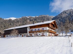 A multi-story building with a snow-covered roof, wooden balconies, and a mountainous backdrop. - Alpenloft on the farm, near Walchsee (Walchsee)