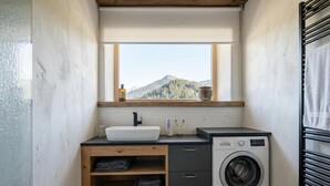 Pequeña lavandería con lavadora, lavabo y ventana con vistas a montañas.