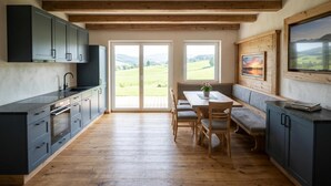 Una cocina moderna con vigas de madera, un comedor con banco y grandes ventanales que ofrecen vistas al campo.