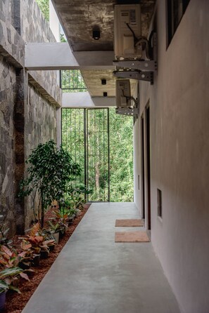 Un pasillo con suelo de concreto, paredes de piedra y plantas en macetas.