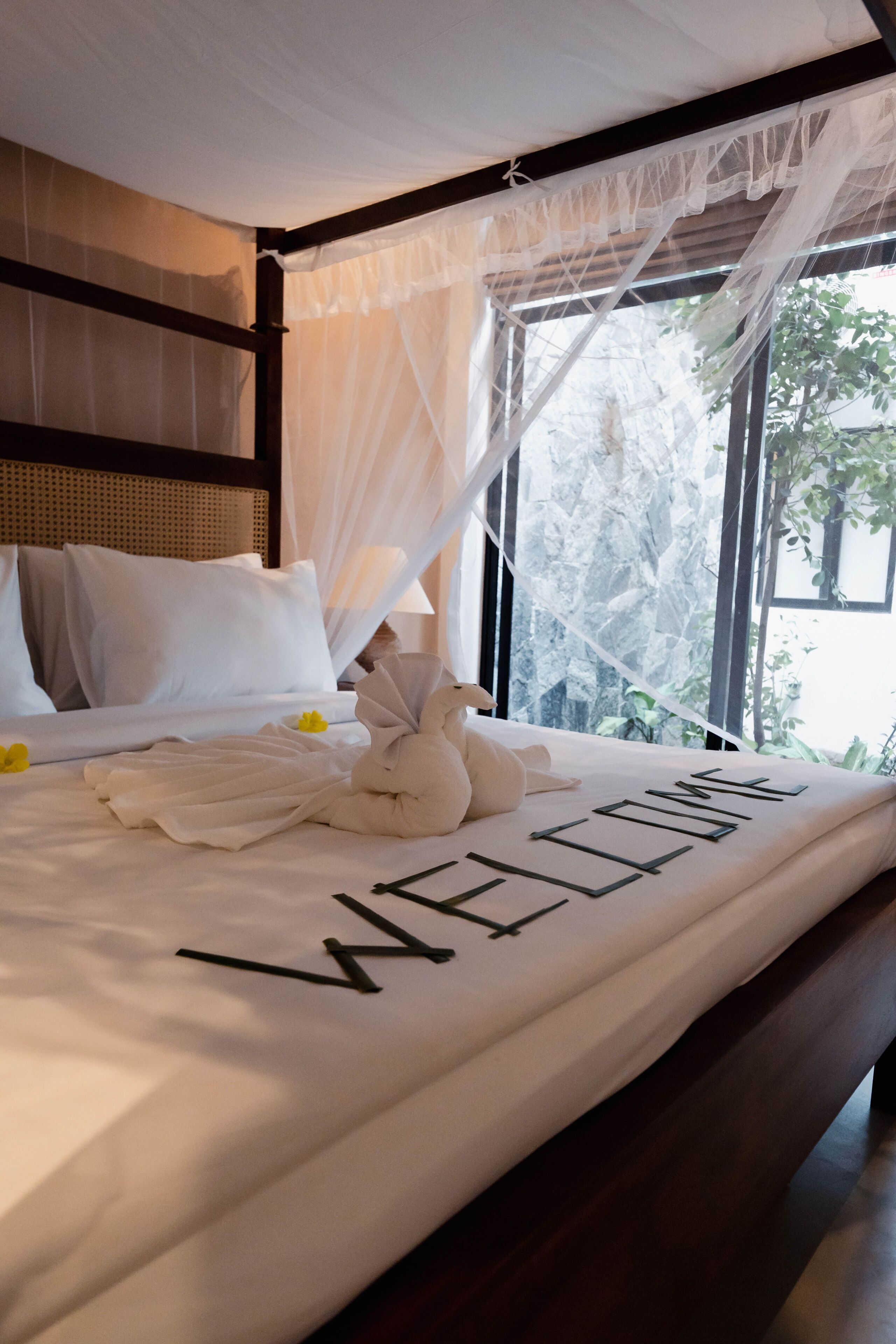 Uma cama com dossel, roupa de cama branca e um tapete de boas-vindas.