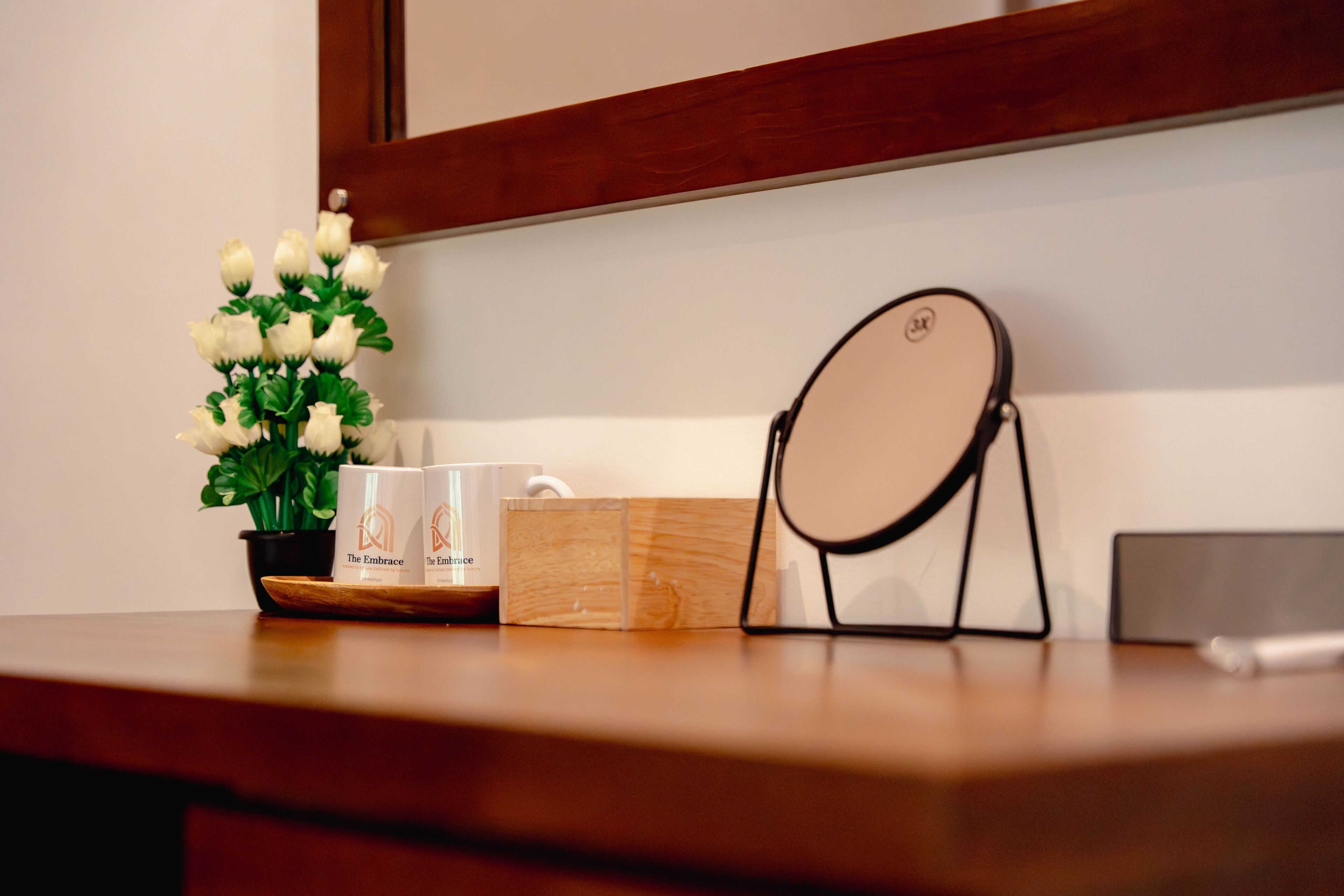 A wooden desk with a potted plant, two mugs, a mirror, and a wooden box.