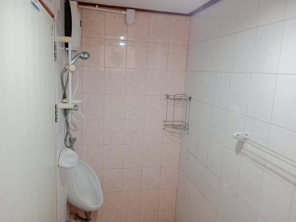 Et lille badeværelse med fliser, urinal, håndklædestang og brusehoved.
