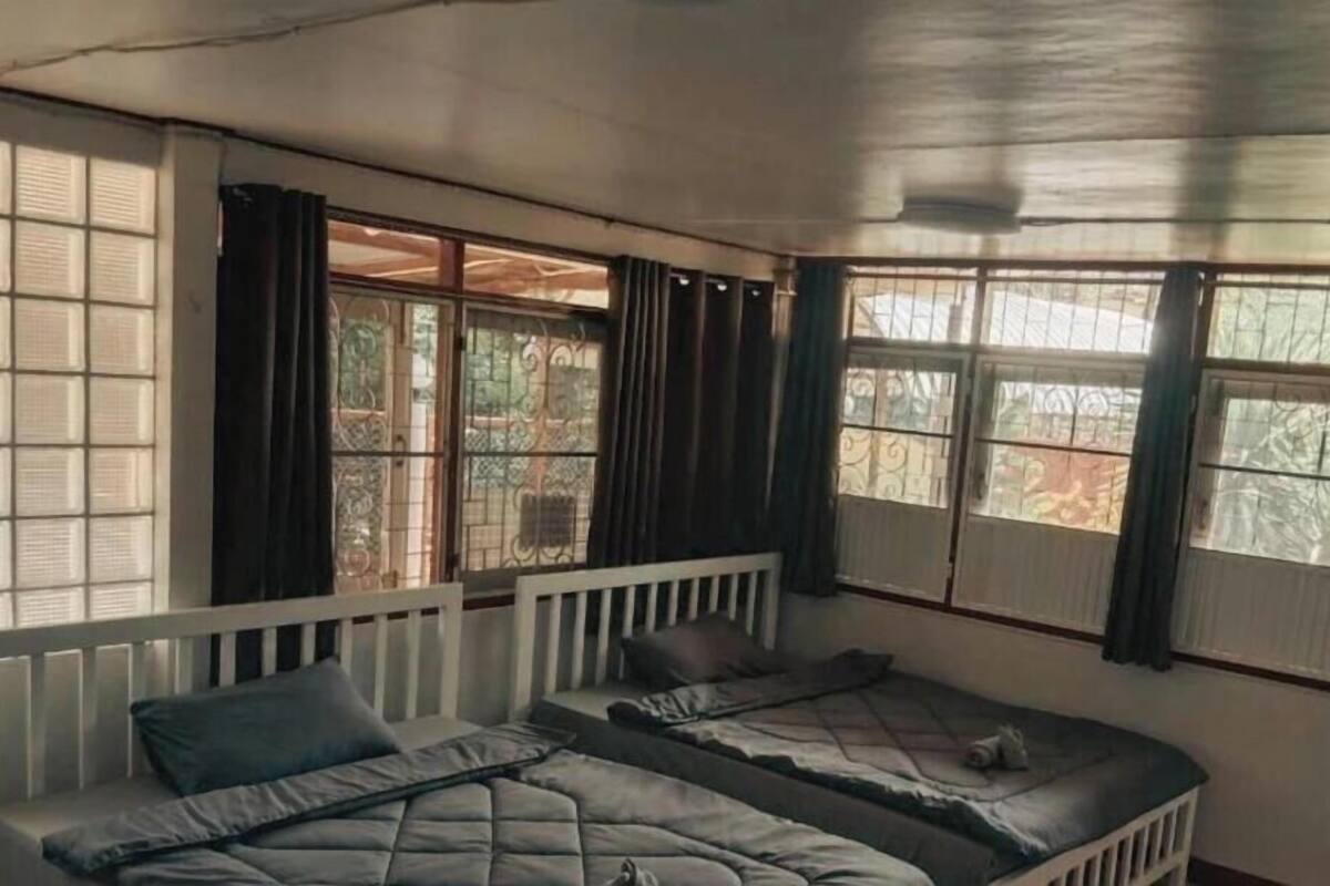 A room with two beds, large windows with curtains, and a radiator.