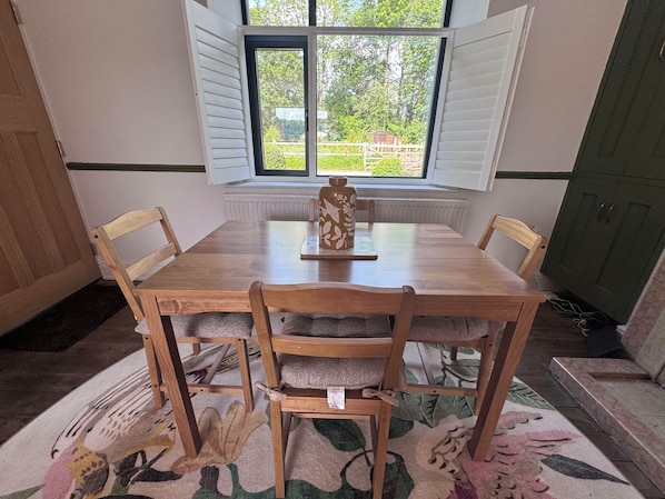 Comedor con mesa y sillas de madera, un florero sobre la mesa y una ventana con contraventanas.