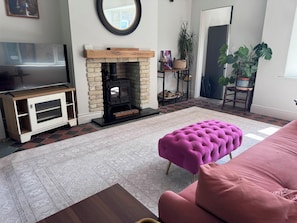 Una sala de estar con chimenea, televisor y un pouf rosa.