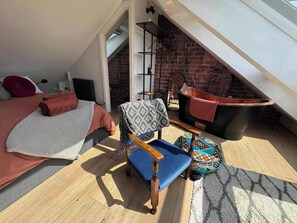 Ein Schlafzimmer im Loft-Stil mit Bett, Sessel, kleinem Tisch, Badewanne und einer Ziegelwand.