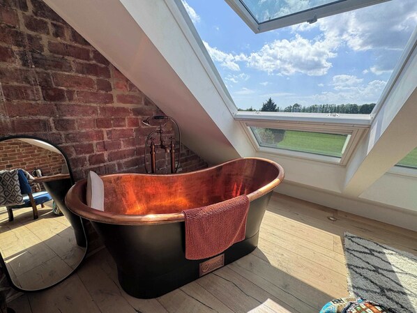 Ein modernes Zimmer mit einem großen Oberlicht, einer Kupferbadewanne und einer Backsteinwand.
