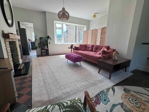 Ein Wohnzimmer mit einem rosafarbenen Sofa, einem gemusterten Teppich, einer hängenden Leuchte und einer Steinwand.