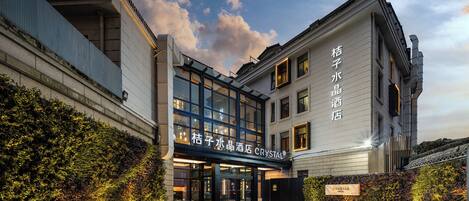 A hotel entrance with a modern design, featuring a glass facade and a signboard.