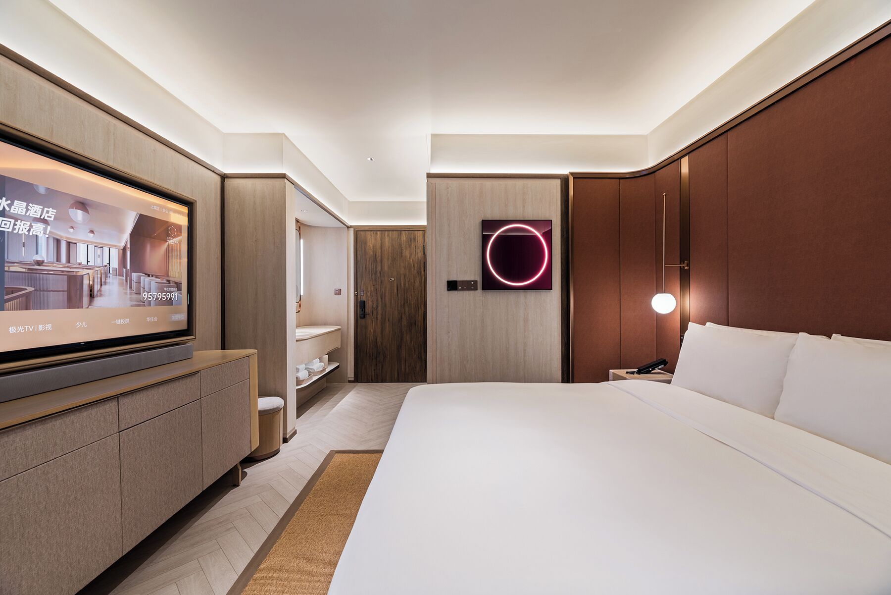 A modern hotel room with a large bed, a TV, a wooden wardrobe, and a circular light fixture.