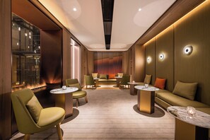 A modern lounge with sofas, chairs, and tables, featuring a glass wall and wooden paneling. - Crystal Hotel Hangzhou Xihu (Hangzhou)