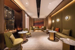 Un salón moderno con sofás, sillones y mesas, que presenta un muro de cristal y paneles de madera.