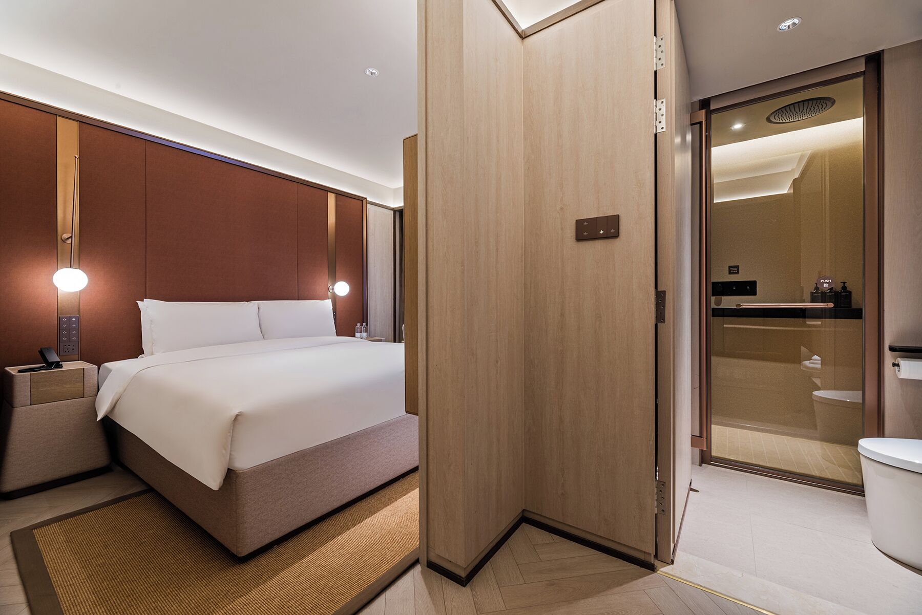 Quarto de hotel com cama, mesa de cabeceira, luminária e banheiro com vaso sanitário e pia.