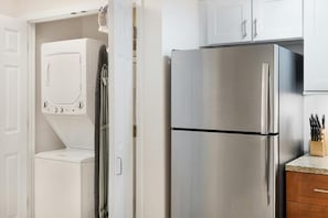 Cozinha equipada com frigorífico de aço inoxidável, máquina de lavar roupa e armários.