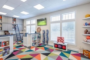 Une piÚce avec un tapis à motifs géométriques, des étagÚres remplies de ballons de sport, un téléviseur et un décor représentant un gouvernail de navire.