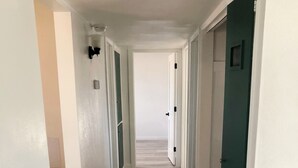 Un corridoio con pavimento in legno, pareti bianche e porte che conducono a diverse stanze.