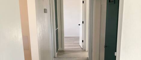 A hallway with wooden flooring, white walls, and doors leading to rooms.