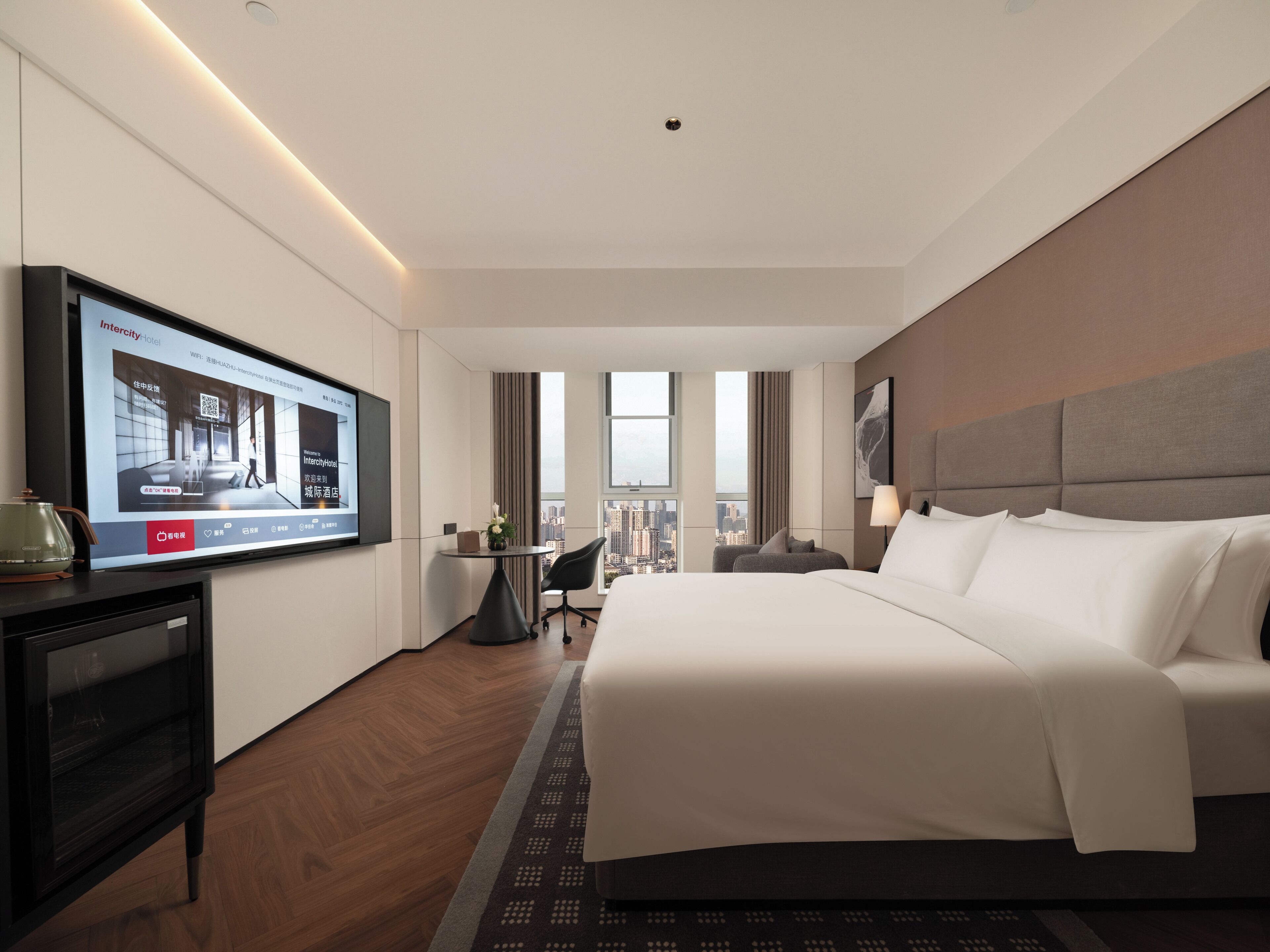 A hotel room with a bed, a desk, a TV, and a view of the city.