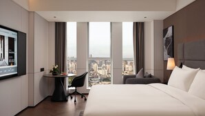 Quarto de hotel com uma cama grande, uma escrivaninha com cadeira, televisão na parede e vista para a cidade.