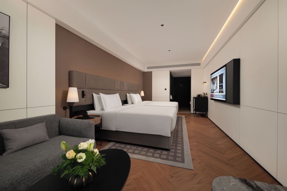 A modern hotel room with a large bed, a sofa, a desk, and a flat-screen TV.