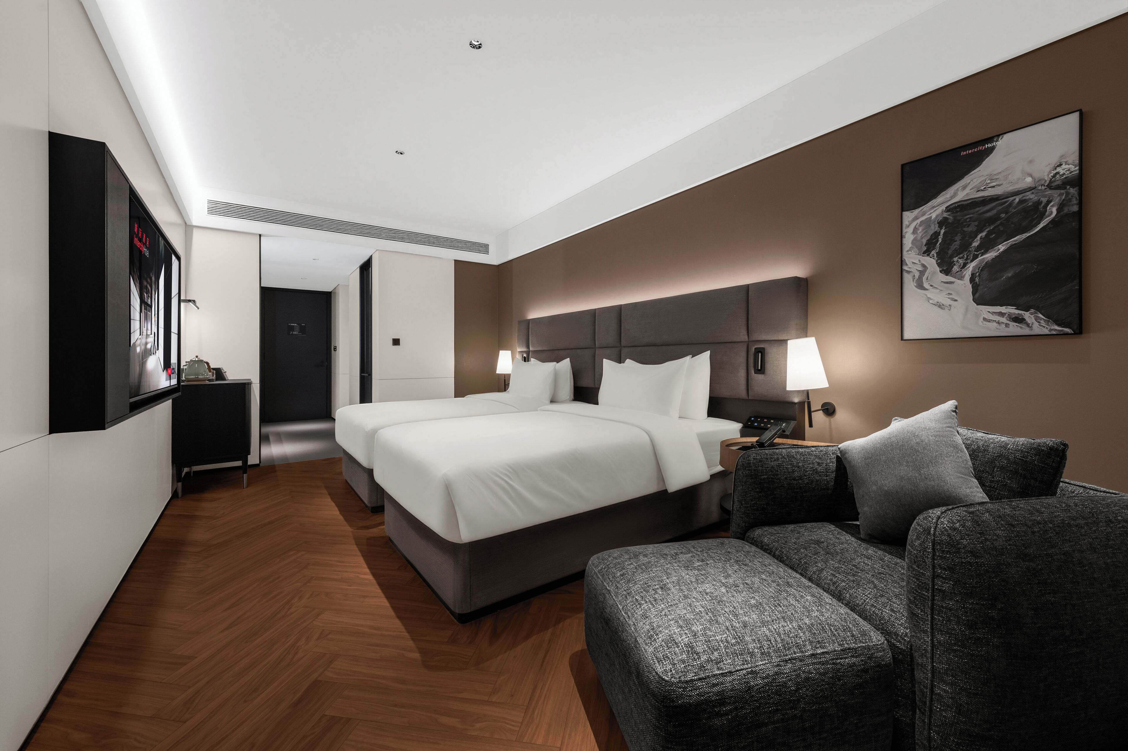 A modern hotel room with a large bed, a sofa, a desk, and a wall-mounted TV.