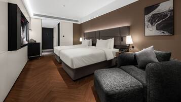 A modern hotel room with a large bed, a sofa, a desk, and a wall-mounted TV.