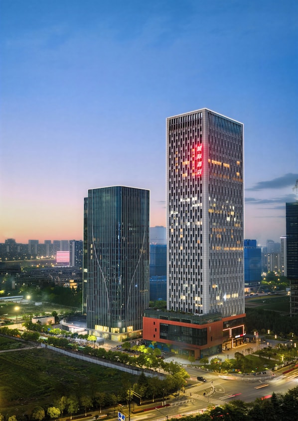 Two high-rise buildings with modern architecture, surrounded by greenery and urban infrastructure.