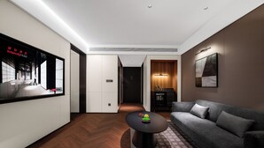 Quarto de hotel moderno com uma televisão de tela plana grande, um sofá, uma mesa de centro e piso de madeira.