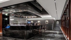 Uma área de bar moderna com um balcão curvo de mármore, diversas opções de assento e um mezanino com prateleiras cheias de garrafas.
