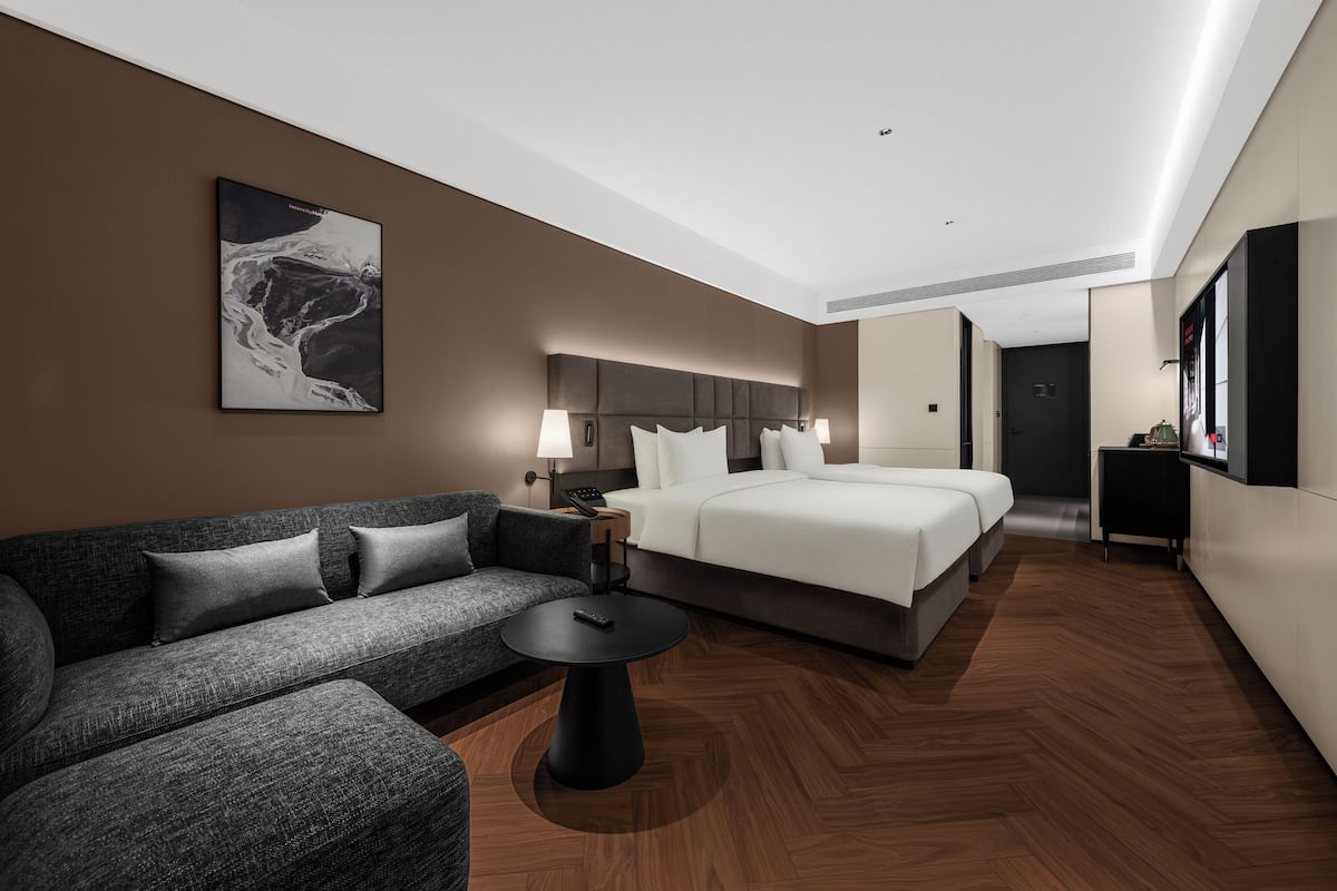 A modern hotel room with a sofa, a bed, a small table, and a painting on the wall.