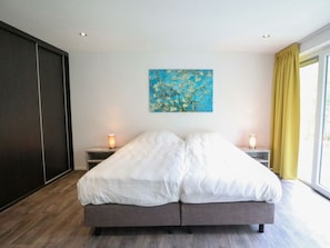 Ein modernes Schlafzimmer mit einem großen Bett, zwei Nachttischen mit Lampen, einem Bild an der Wand und Blick durch ein Fenster mit Vorhängen.