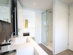Ein modernes Badezimmer mit einer Duschkabine aus Glas, einem großen Spiegel und einem weißen Waschbecken.
