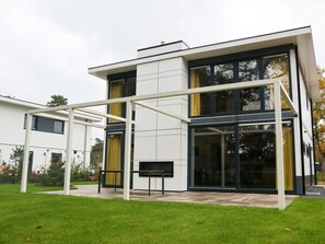 Ein modernes, zweistöckiges Haus mit Terrasse, großen Fenstern und einer Pergola.