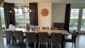 Un espace repas moderne avec une grande table en bois, plusieurs chaises, une horloge au mur et de grandes fenêtres avec des rideaux.