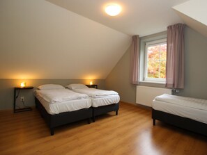 Een slaapkamer met twee bedden, een raam met gordijnen, een radiator en een plafondlamp.
