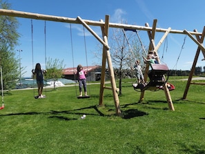 A wooden swing set in a grassy area with a clear sky. - Vacation Apartment (Courtyard Side) for up to 4 people, balcony, 65 square meters (Taching am See)