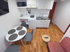 A compact kitchen with a microwave, sink, and small refrigerator. There is a dining table with chairs and a red sofa. - Mini Home | Fully equipped | With elevator (Cusco)
