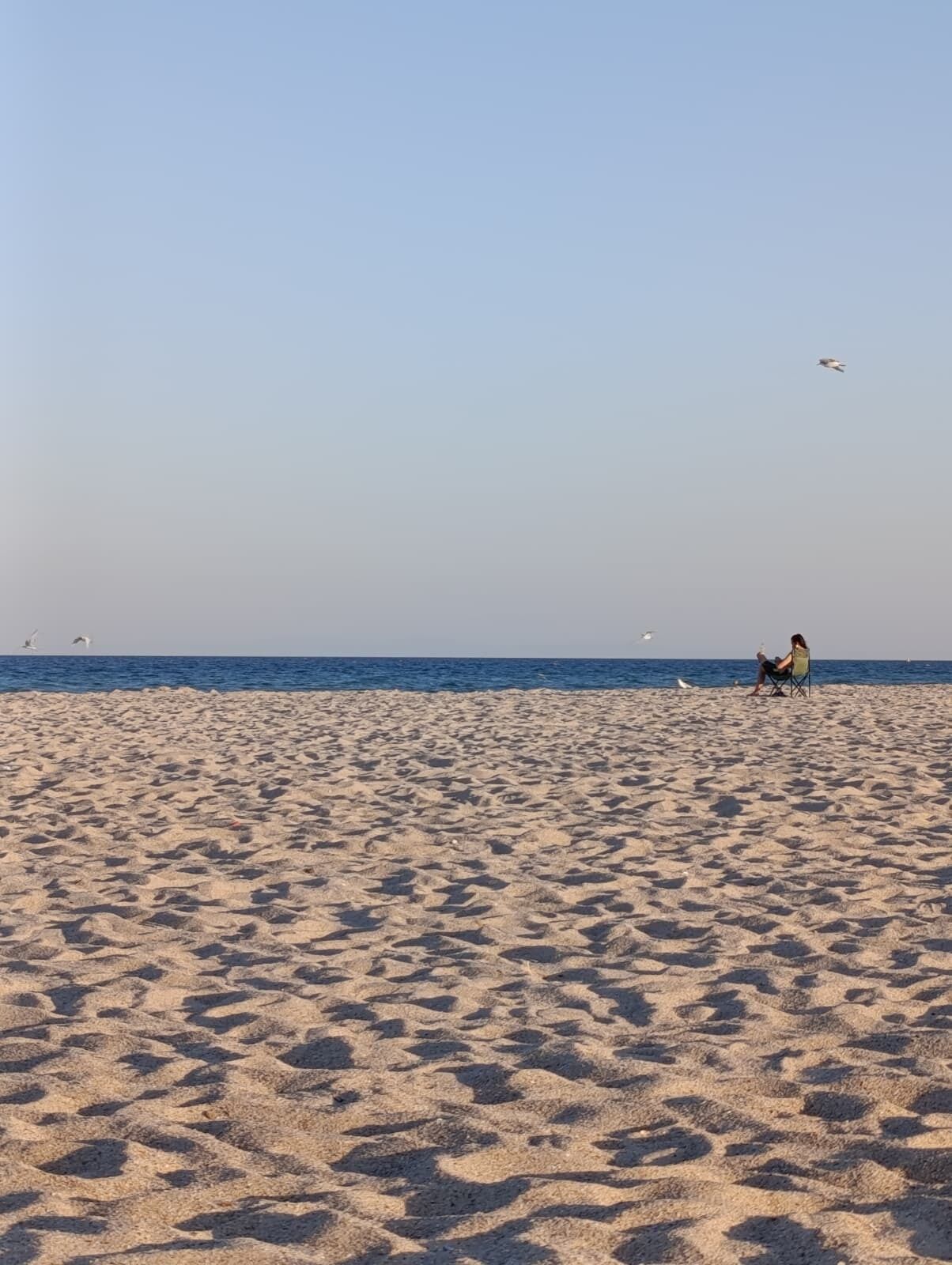 A wide sandy beach with a clear sky and a person sitting in a chair.