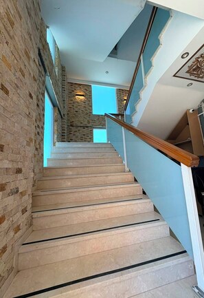 Una escalera con un muro de ladrillo a un lado y un muro azul al otro, que lleva a un piso superior.
