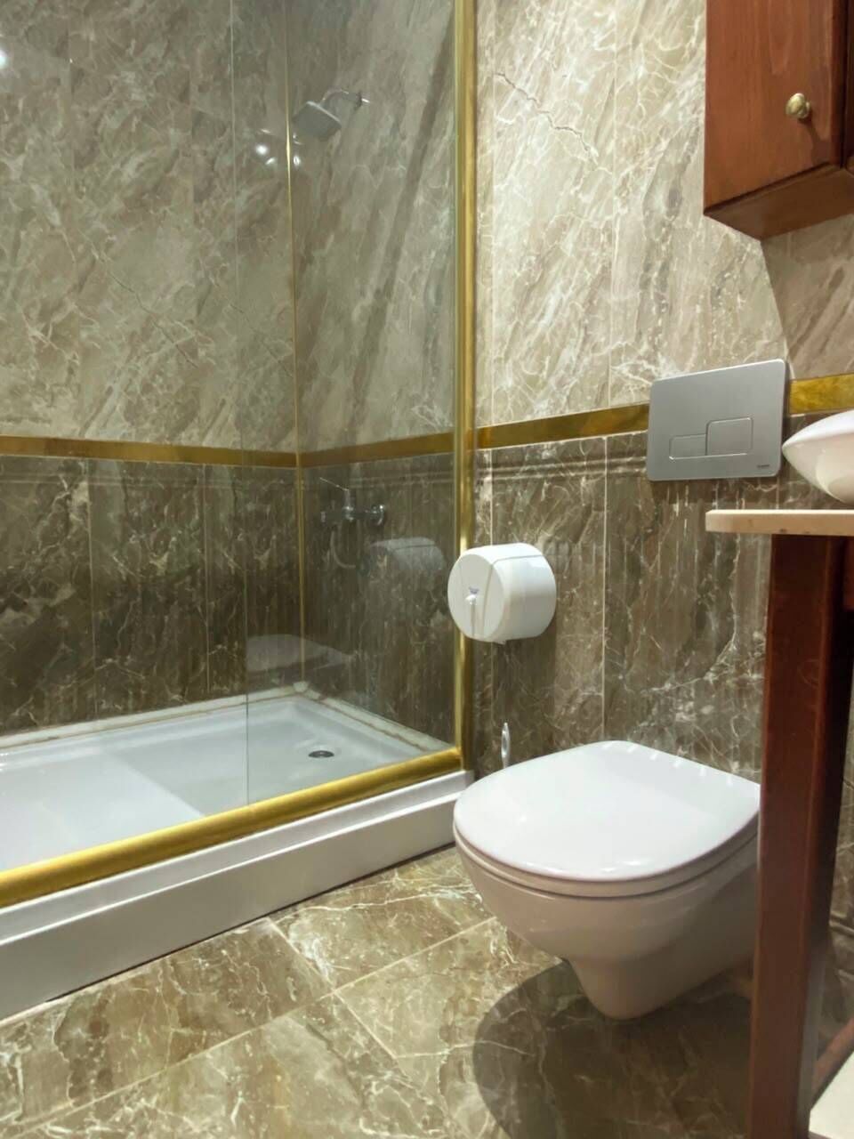 Un baño con cabina de ducha de vidrio, inodoro y piso de mármol.