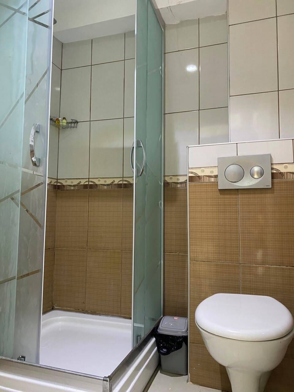 A bathroom with a glass-enclosed shower, a toilet, and a trash bin.