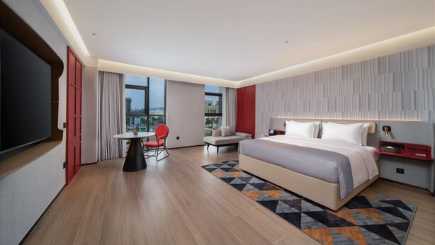 A modern hotel room with a large bed, a small table, a red chair, and a TV. - Wanda Moments Bengbu south Railway (Bengbu)