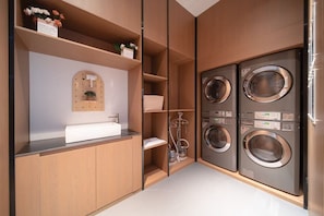 Un moderno lavadero equipado con lavadoras y secadoras integradas, un lavabo y un espejo.
